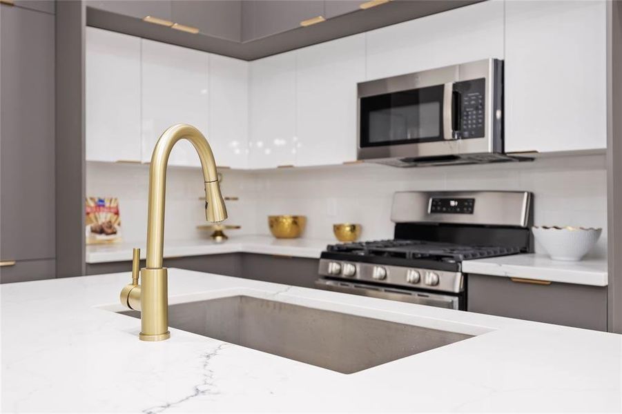 Clean lines, a large island, and brushed gold fixtures provide a sleek and modern space. Abundant cabinets over and under the counters and pantry provide for plenty of storage.