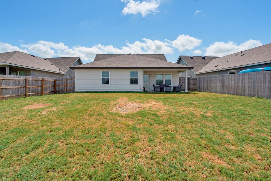 A fully fenced backyard features a covered back porch and a generous lawn area. A fully fenced backyard features a covered back porch and a generous lawn area.