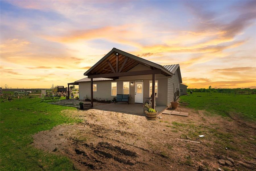 Back of house at dusk featuring a yard, metal roof, and a patio area
