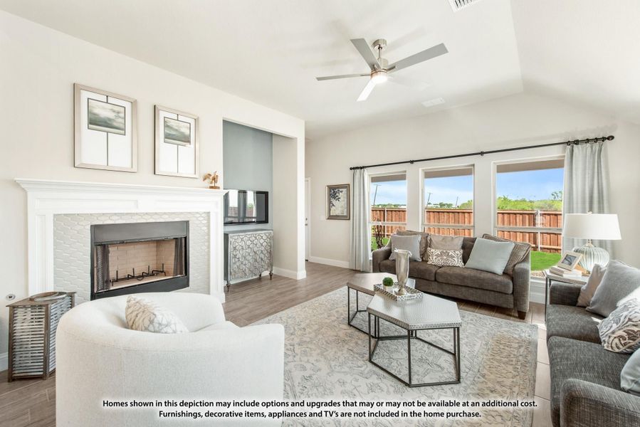 Living room with vaulted ceiling, white fireplace, ceiling fan, and large windows overlooking backyard Living room with vaulted ceiling, white fireplace, ceiling fan, and large windows overlooking backyard