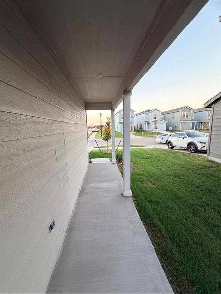 Covered concrete porch with white support columns, wood-finish siding, and a recessed ceiling light Covered concrete porch with white support columns, wood-finish siding, and a recessed ceiling light