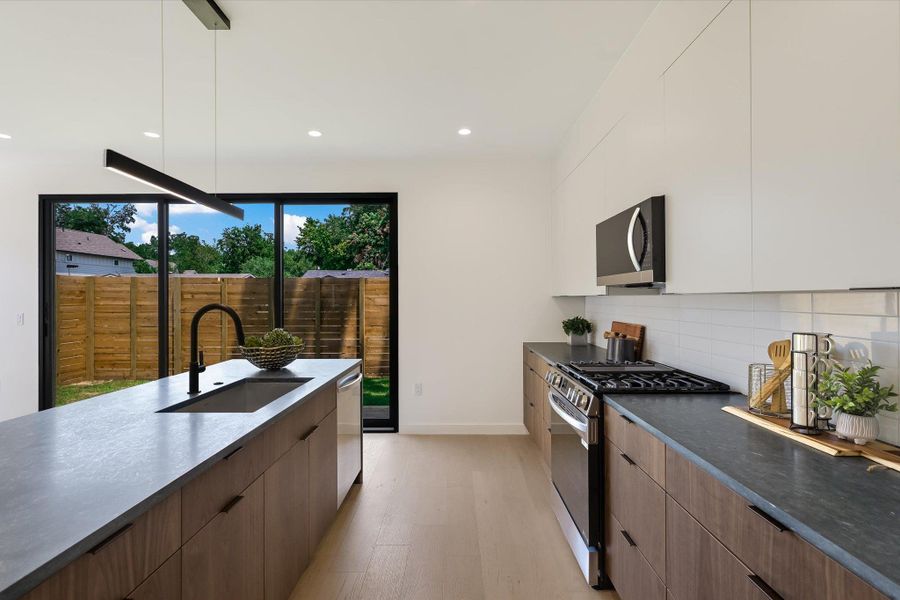 Kitchen with modern cabinets, appliances with stainless steel finishes, light wood finished floors, dark countertops, and decorative backsplash