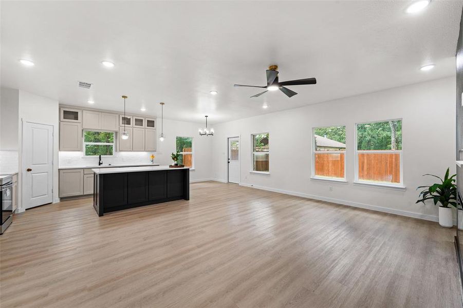 Open-concept living space featuring wood-finish flooring, a contemporary kitchen island with a dark finish, light-toned cabinetry, and recessed lighting Open-concept living space featuring wood-finish flooring, a contemporary kitchen island with a dark finish, light-toned cabinetry, and recessed lighting
