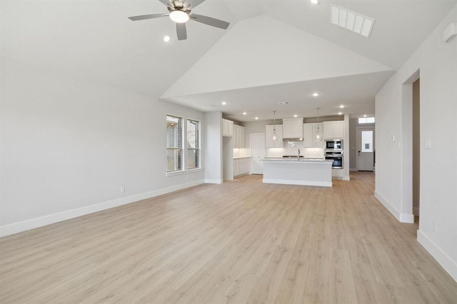 Unfurnished living room with light wood finished floors, recessed lighting, high vaulted ceiling, and ceiling fan