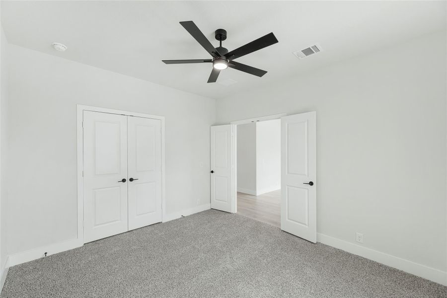 Empty bedroom with gray carpet, black ceiling fan, and white double closet doors