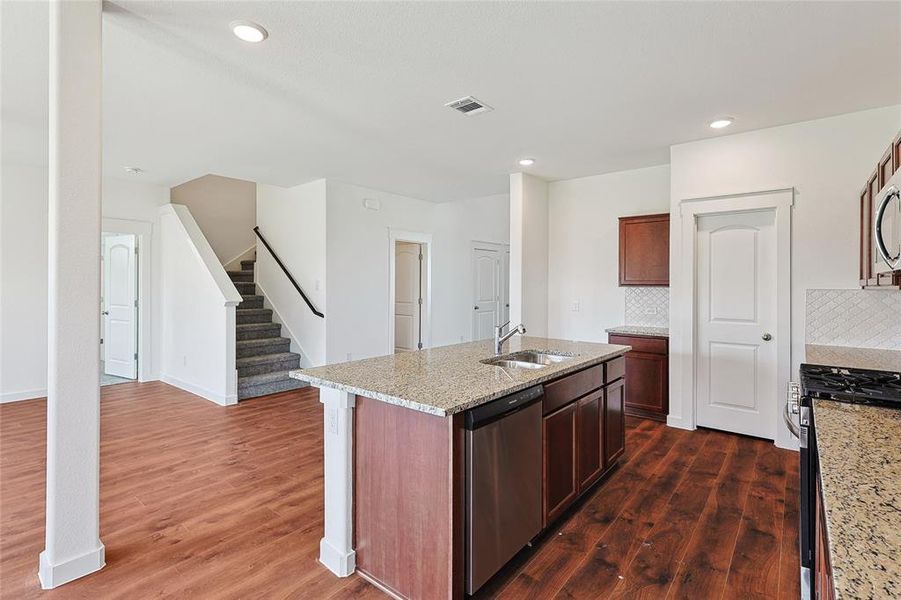 Kitchen with stainless steel appliances, light stone counters, a center island with sink, tasteful backsplash, and dark wood finished floors
