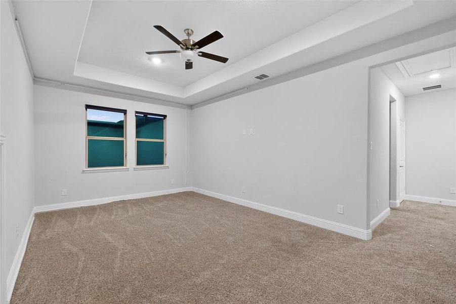 Unfurnished room featuring a tray ceiling, light carpet, ceiling fan, and attic access