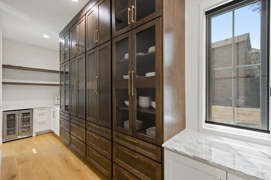 Custom cabinetry and warm hardwood flooring define this well-appointed pantry, featuring a wine cooler and expansive storage. Custom cabinetry and warm hardwood flooring define this well-appointed pantry, featuring a wine cooler and expansive storage.