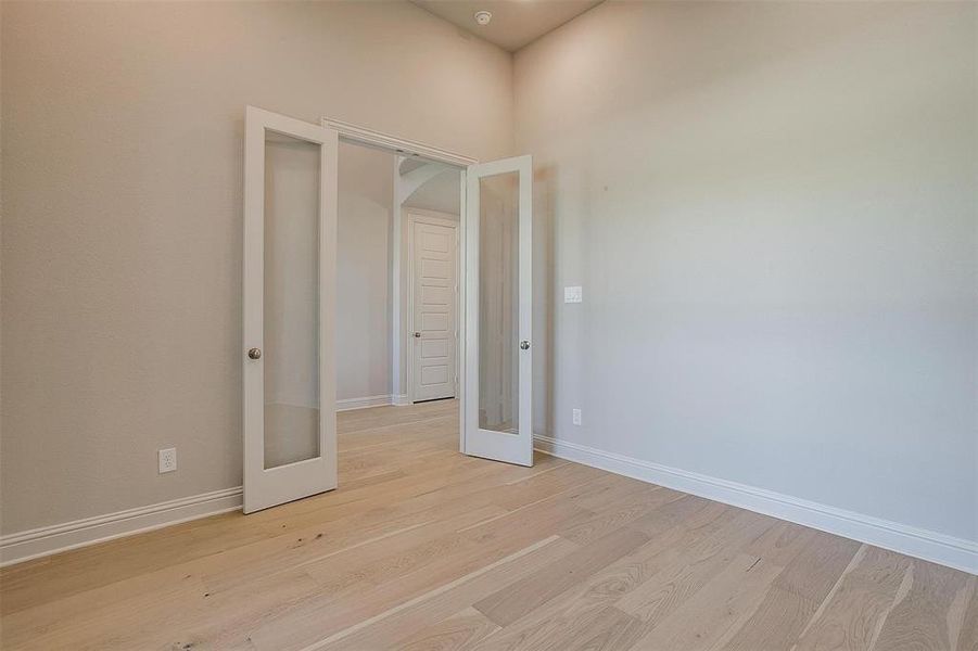 Empty room featuring light hardwood / wood-style flooring, a high ceiling, and french doors