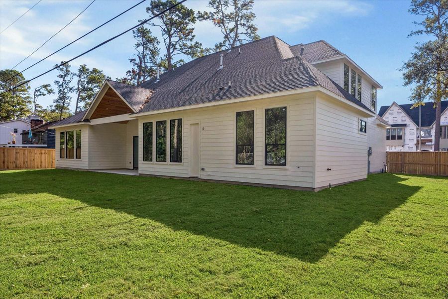 Back exterior view with covered patio, tall windows, and a generous fenced yard.