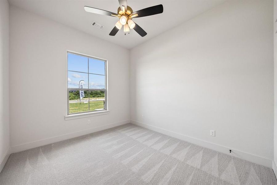 Room featuring a ceiling fan with integrated lighting, a large window with white trim, light-toned walls, and patterned carpet flooring