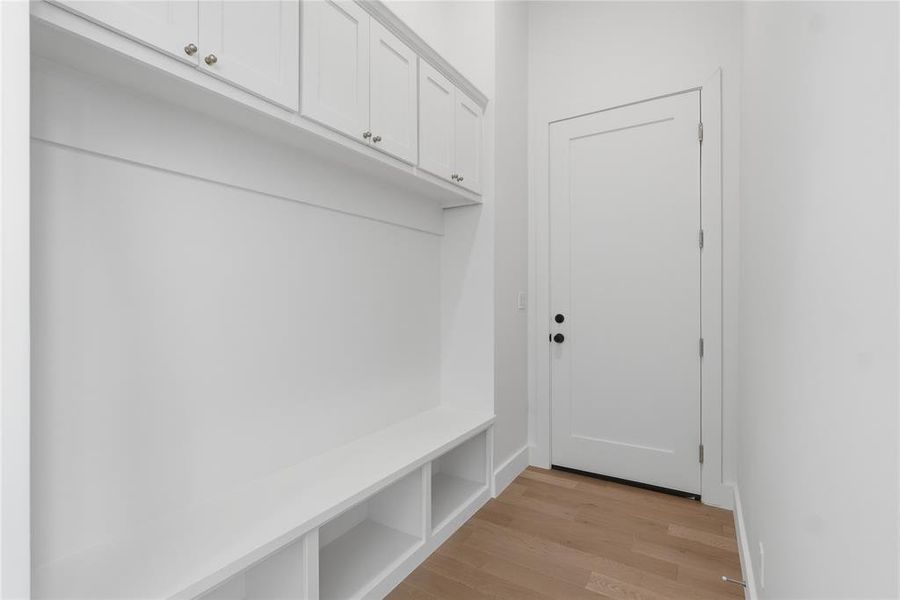 Built-in mudroom bench with cubby storage, upper cabinetry with brushed nickel hardware, and wood-finish flooring