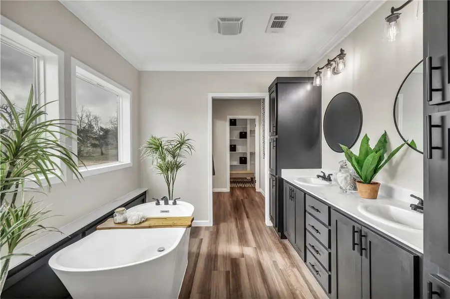 Full bath featuring a soaking tub, crown molding, double vanity, and dark wood finished floors