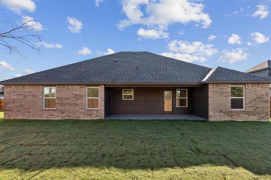 Rear view of house featuring a patio, a yard, and roof with shingles