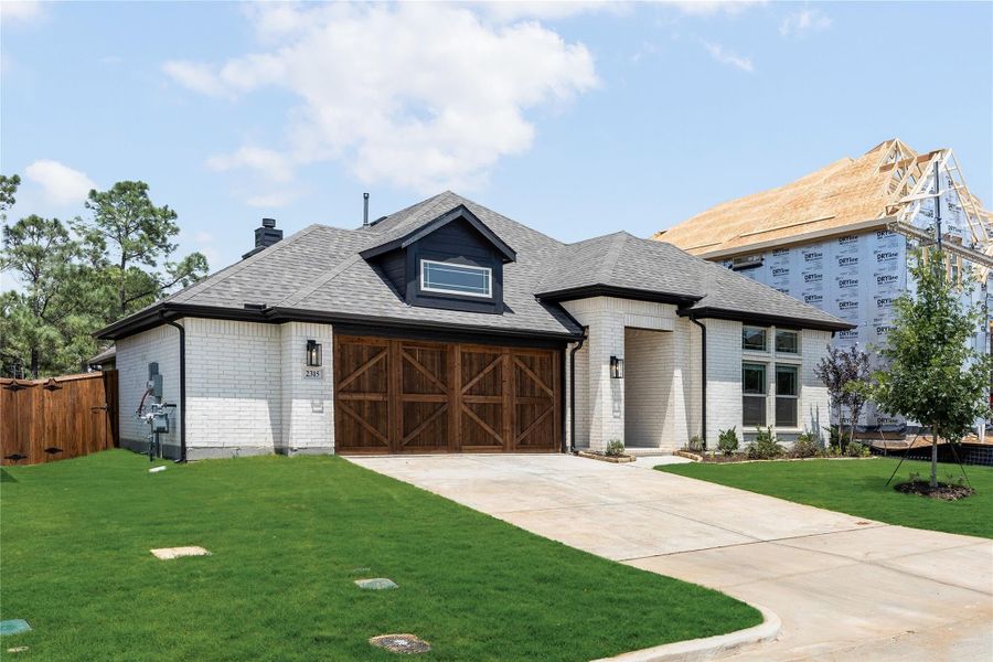 Single-story home with white brick exterior, wood garage doors, and green front lawn