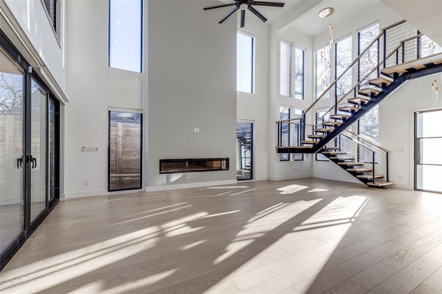 Living room with fireplace, grand stairway, light wood flooring, and custom electric shades