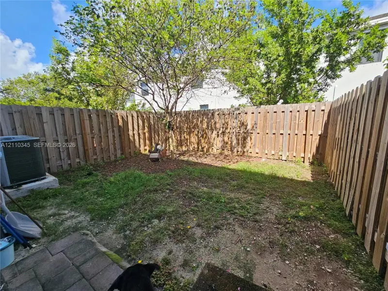 Fenced backyard featuring vertical wood-plank fencing, paver hardscaping, and mature trees