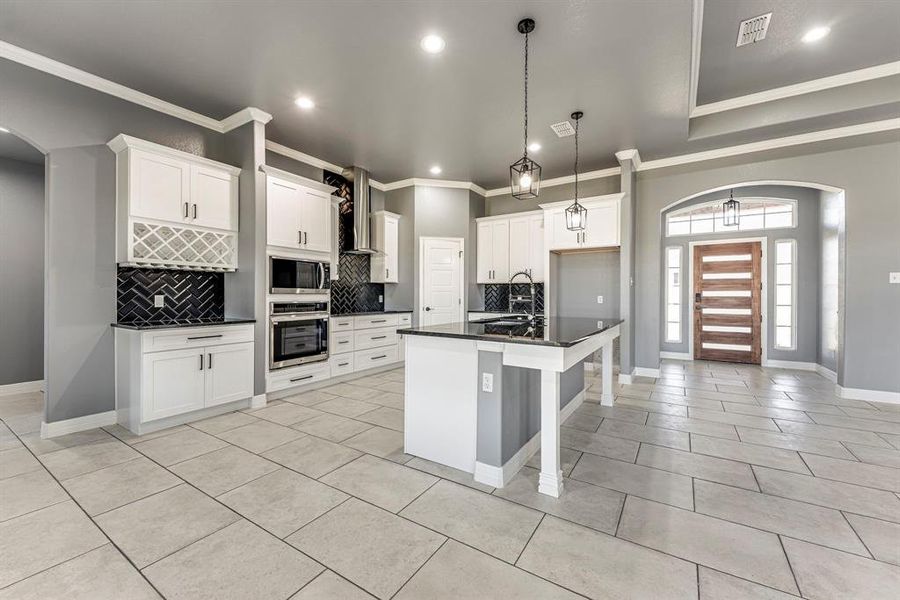 Kitchen with a center island with sink, white cabinets, wall chimney range hood, decorative backsplash, and appliances with stainless steel finishes