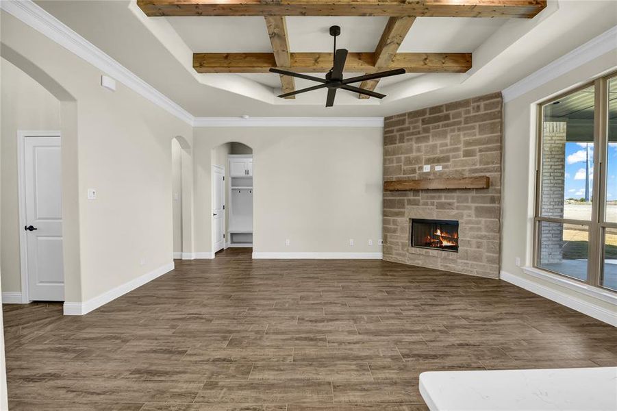 Unfurnished living room with beam ceiling, dark wood-type flooring, and a stone fireplace