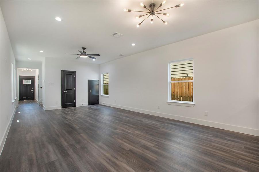 Unfurnished living room with ceiling fan with notable chandelier and dark hardwood / wood-style flooring