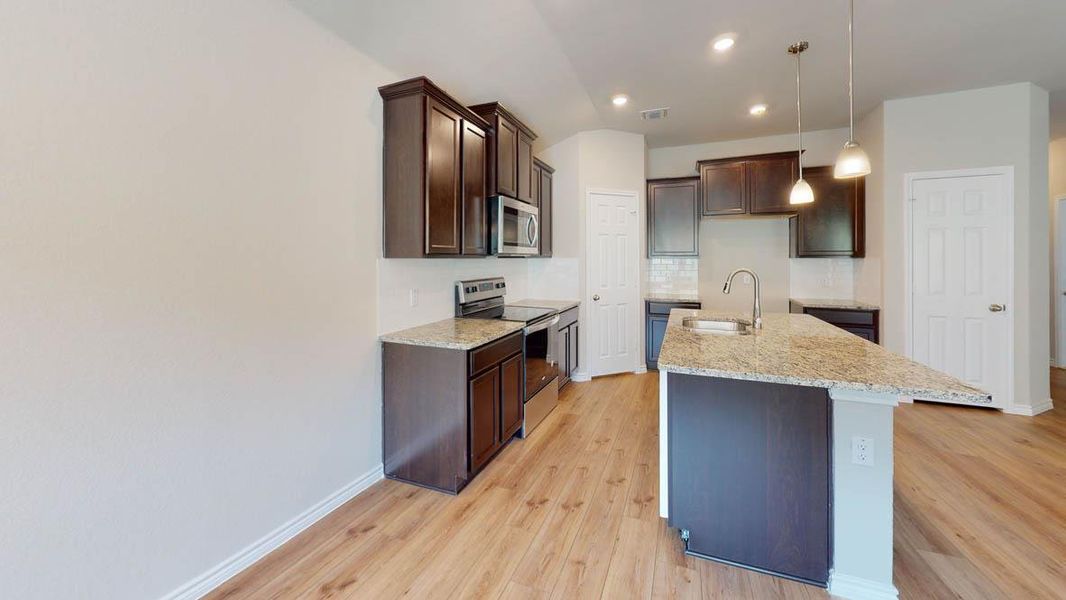 Kitchen with stainless steel appliances, dark wood finish cabinets, light stone countertops, light wood finished floors, and a kitchen island with sink