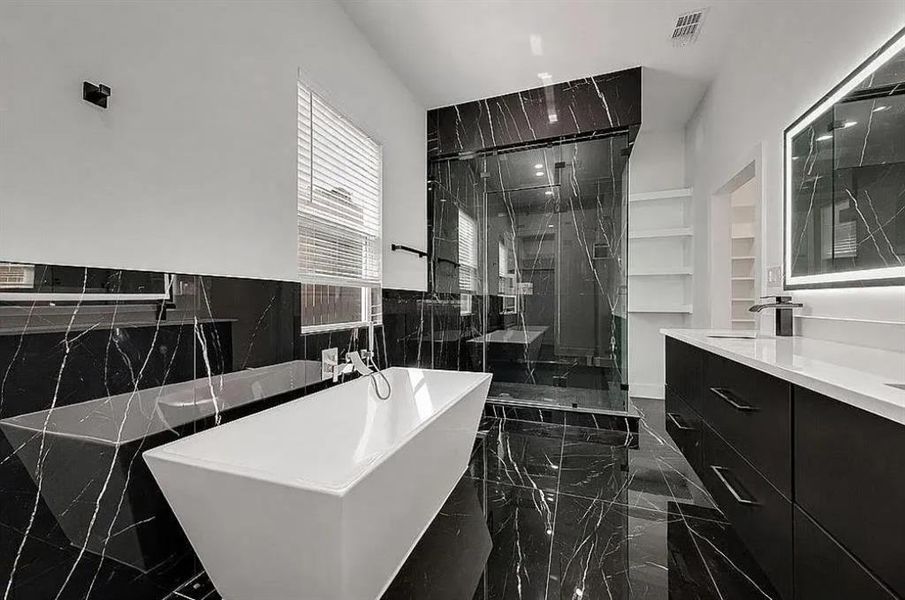 Modern bathroom featuring a freestanding soaking tub with wall-mounted faucet, a spacious glass-enclosed shower, black marble-look tile flooring and walls, a double vanity with integrated sinks and quartz countertops, and an illuminated mirror