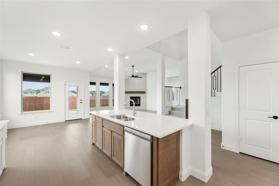 Kitchen island with sink, stainless dishwasher, and white countertop, open to living area with fireplace and hardwood floors Kitchen island with sink, stainless dishwasher, and white countertop, open to living area with fireplace and hardwood floors