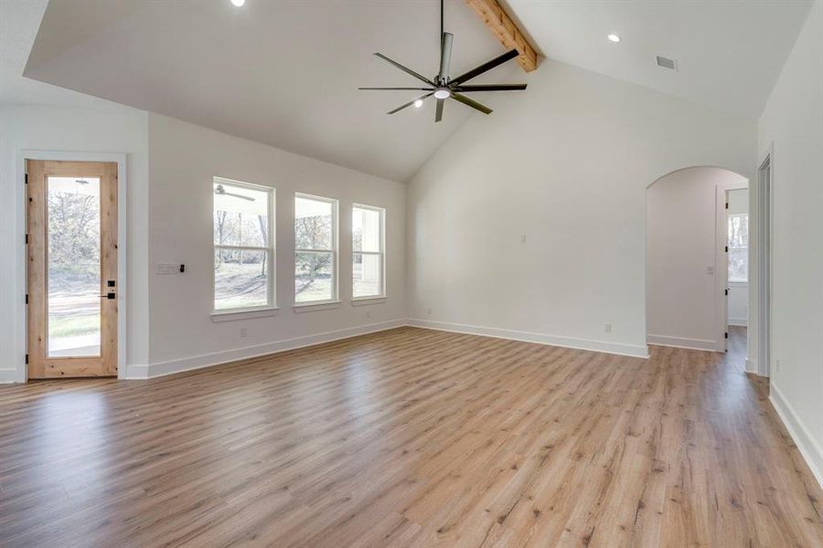 Unfurnished living room featuring ceiling fan, light hardwood / wood-style floors, high vaulted ceiling, and beamed ceiling