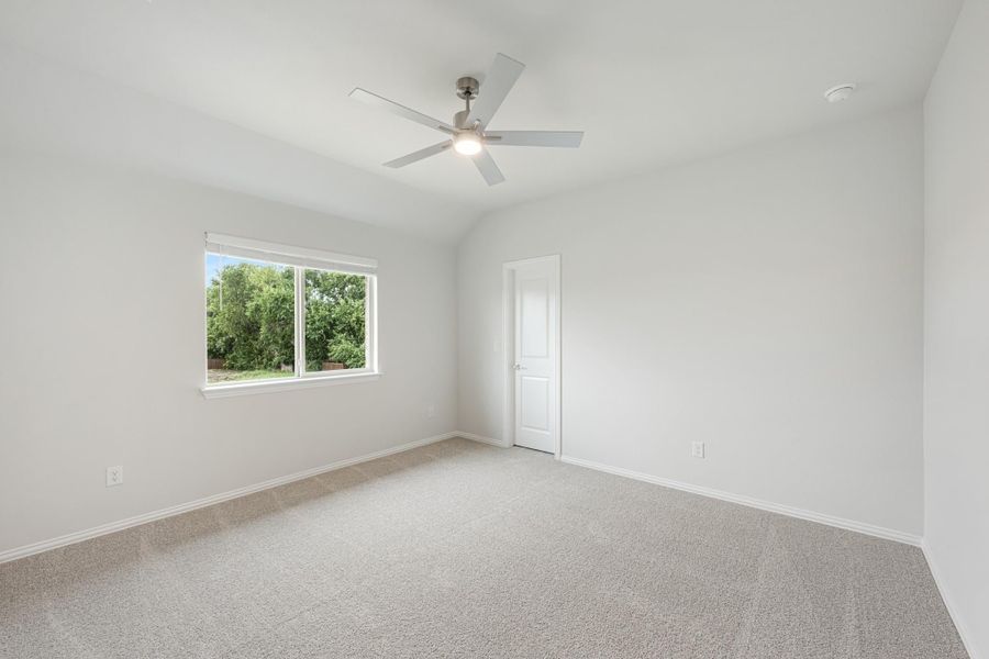 Empty bedroom with vaulted ceiling, ceiling fan, carpet flooring, and a window with backyard view Empty bedroom with vaulted ceiling, ceiling fan, carpet flooring, and a window with backyard view