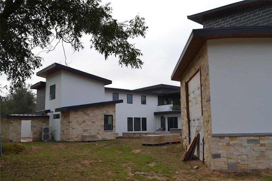 Rear view of house with stucco siding, stone siding, a lawn, and a patio area Rear view of house with stucco siding, stone siding, a lawn, and a patio area