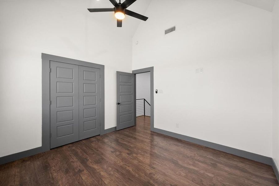 Unfurnished bedroom featuring ceiling fan, high vaulted ceiling, visible vents, baseboards, and dark wood-style floors Unfurnished bedroom featuring ceiling fan, high vaulted ceiling, visible vents, baseboards, and dark wood-style floors