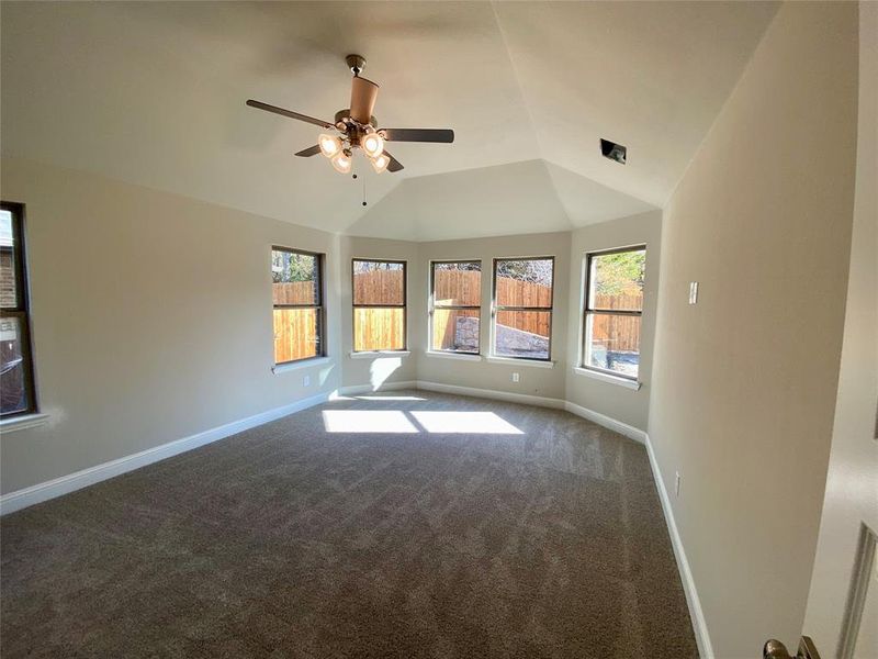 Large master bedroom featuring bay window with plenty of natural light, vaulted ceiling, and ceiling fan.