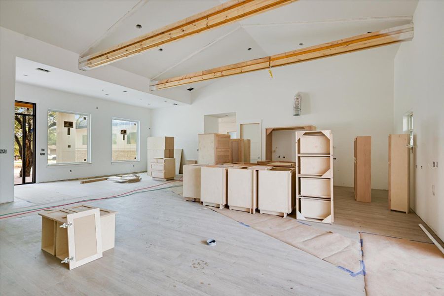 Unfinished kitchen with beamed ceiling, light flooring and cabinets being installed