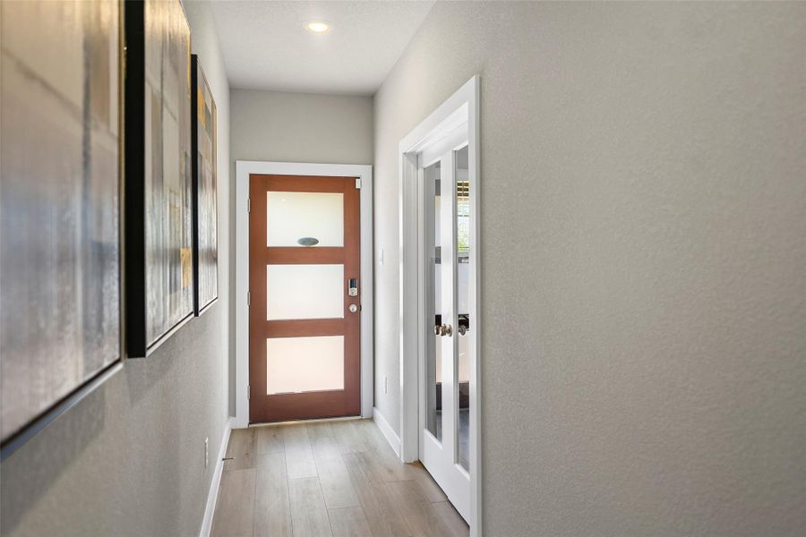 Bright and inviting hallway with modern wood and glass front door, complemented by sleek flooring.