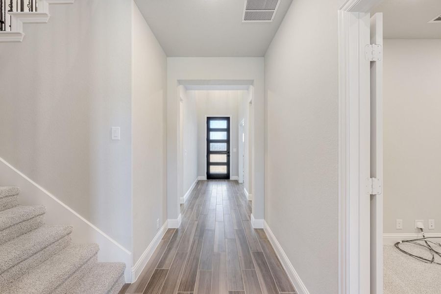 Hallway with wood-look tile floors, white walls, and black front door with glass panels, staircase on left Hallway with wood-look tile floors, white walls, and black front door with glass panels, staircase on left