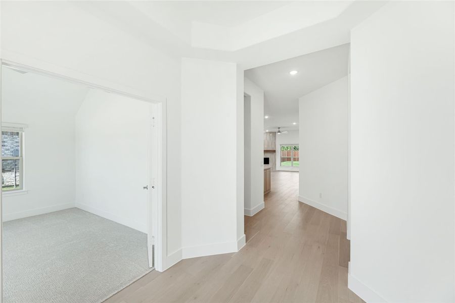 Hallway with light hardwood floors and white walls leading to open living area with ceiling fan