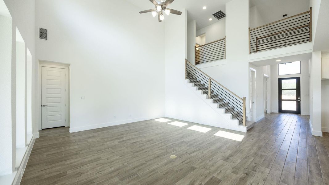 Unfurnished living room with a high ceiling, stairway, wood finished floors, ceiling fan, and baseboards Unfurnished living room with a high ceiling, stairway, wood finished floors, ceiling fan, and baseboards