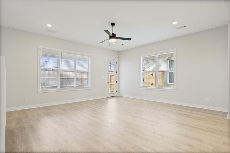 Spacious room featuring light wood-finish flooring, white walls, and multiple windows Spacious room featuring light wood-finish flooring, white walls, and multiple windows