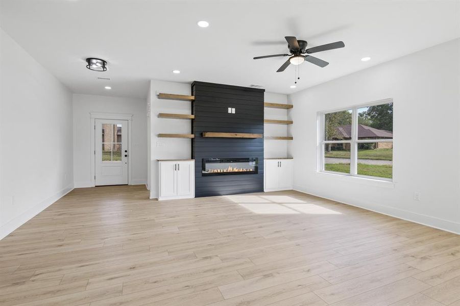 Unfurnished living room with a large fireplace, recessed lighting, ceiling fan, and light wood-style flooring