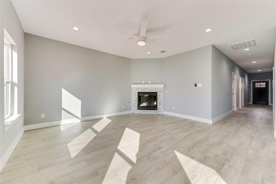 Unfurnished living room with light hardwood / wood-style flooring, a stone fireplace, a wealth of natural light, and ceiling fan