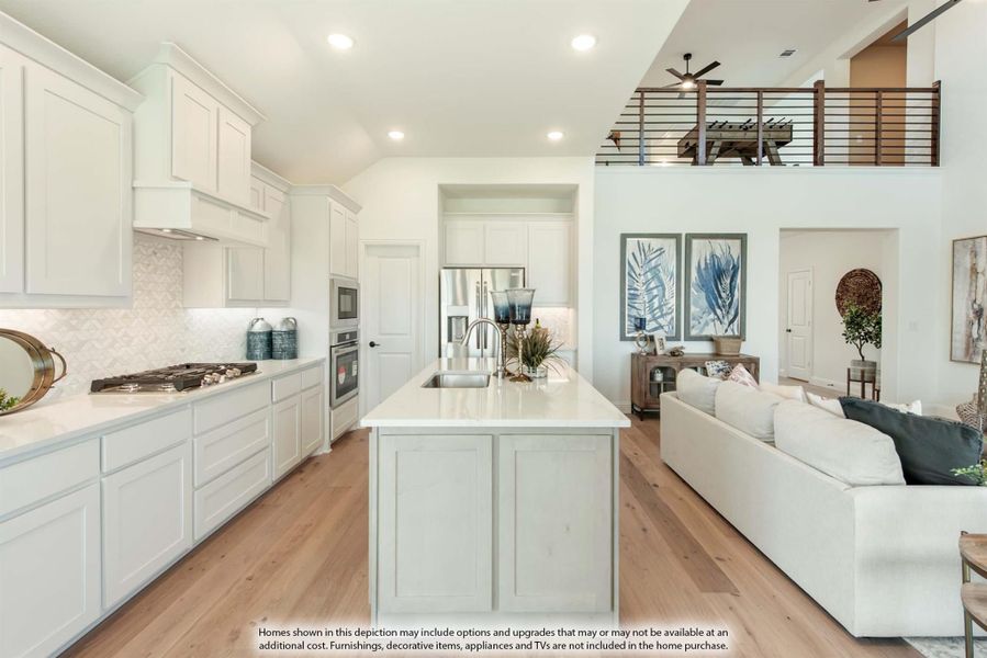 Open-concept kitchen with white cabinets, large island, and hardwood floors opening to living area with second-floor loft above