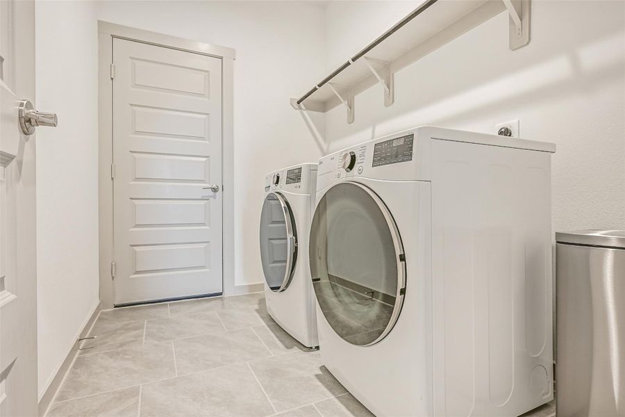 The spacious interior utility room accommodates full-size side-by-side laundry appliances and features easy-care tile flooring plus a long shelf and hanging rod for added storage and functionality. The spacious interior utility room accommodates full-size side-by-side laundry appliances and features easy-care tile flooring plus a long shelf and hanging rod for added storage and functionality.