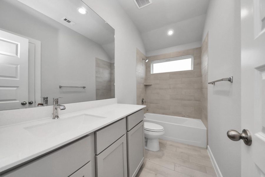Secondary bath features tile flooring, bath/shower combo with tile surround, light stained wood cabinets, beautiful light countertop.