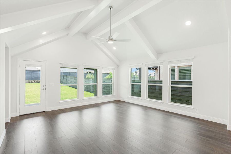 Bright empty living room with vaulted beamed ceiling, ceiling fan, dark hardwood floors, and large windows overlooking backyard Bright empty living room with vaulted beamed ceiling, ceiling fan, dark hardwood floors, and large windows overlooking backyard