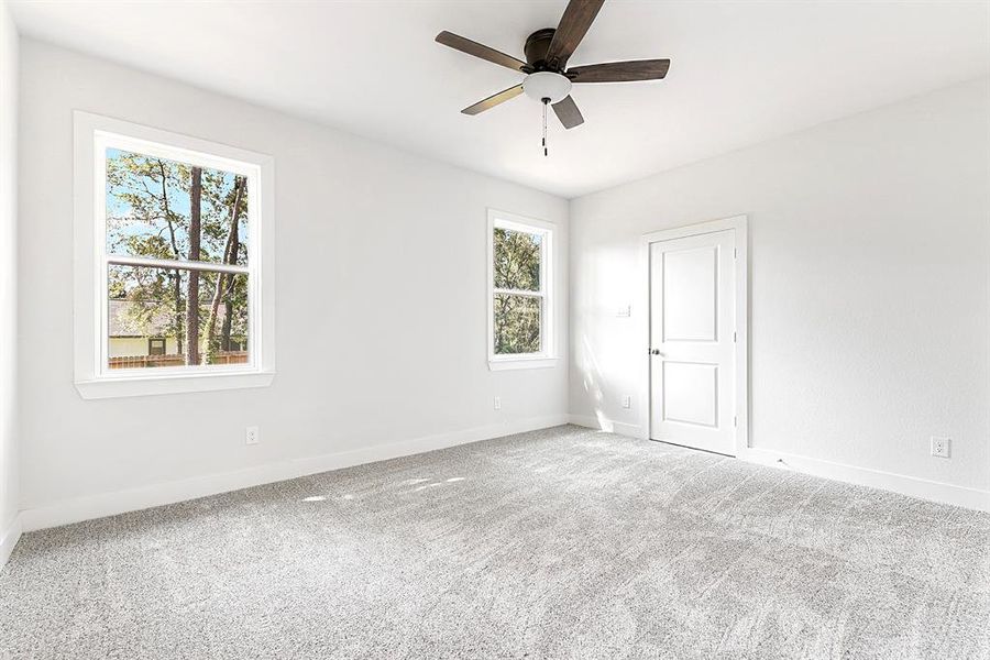 Primary bedroom with lots of natural lighting, ceiling fan, light gray carpet.