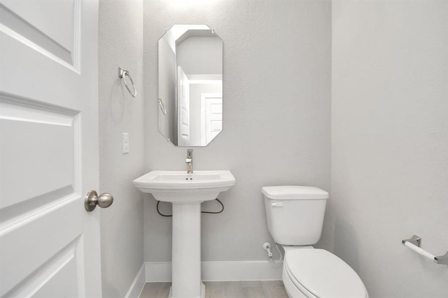 This half bathroom features a stylish pedestal sink, modern hardware, and bright recessedlighting, creating a sleek and inviting space.