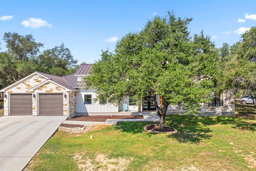 View of front of house featuring a metal roof, stone siding, a standing seam roof, a front lawn, and driveway
