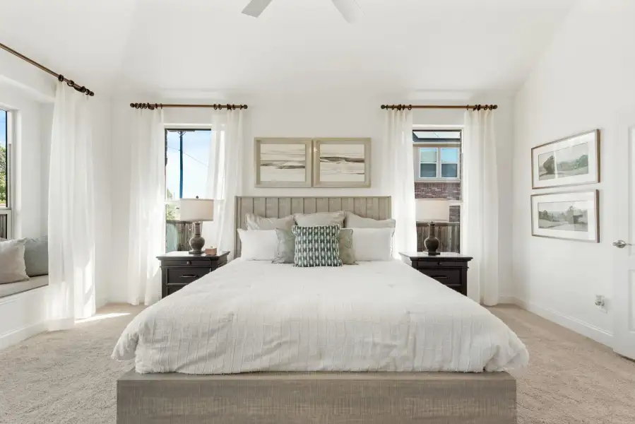 Bright master bedroom with king bed, vaulted ceiling, carpet floors, and multiple windows with white curtains