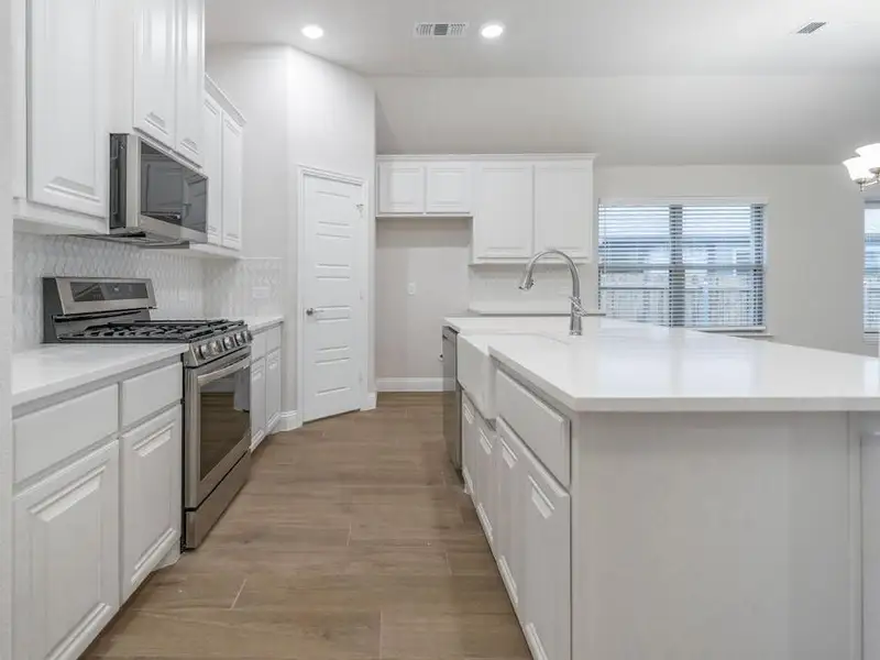 Kitchen featuring white cabinets, light wood-type flooring, an island with sink, tasteful backsplash, and stainless steel appliances