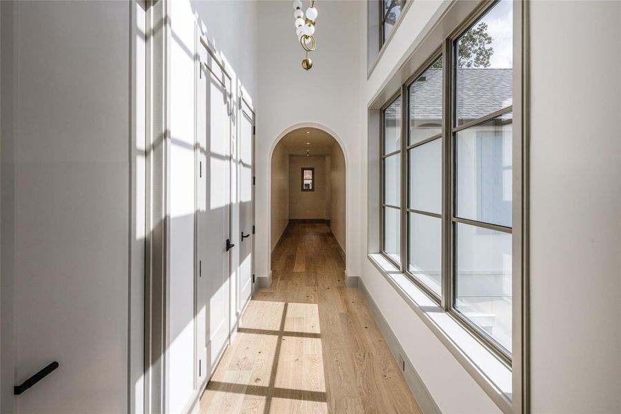 Natural light steals the show upstairs. Oversized windows flood the hall from both sides, while a sculptural chandelier draws the eye through the arched opening beyond. Even the hallway gets a moment.